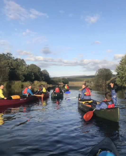 Group of students canoeing along a scenic river surrounded by trees under a bright blue sky. Group of students canoeing along a scenic river surrounded by trees under a bright blue sky.
